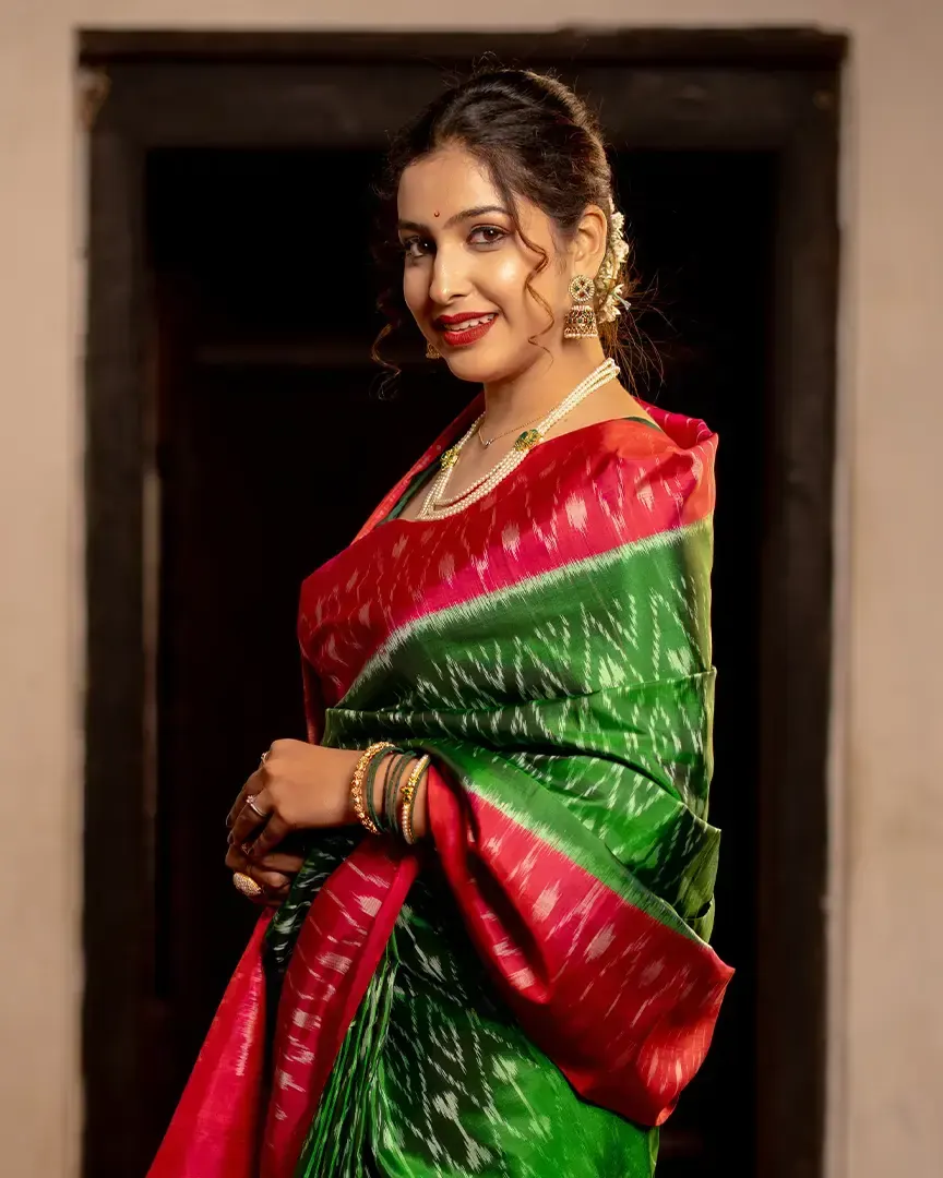 Model in a green and red silk saree in a doorway